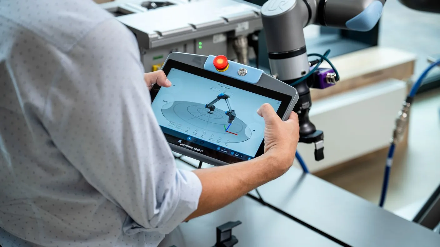 An operator programming a Universal Robots arm on the TP7 teach pendant running PolyScope X