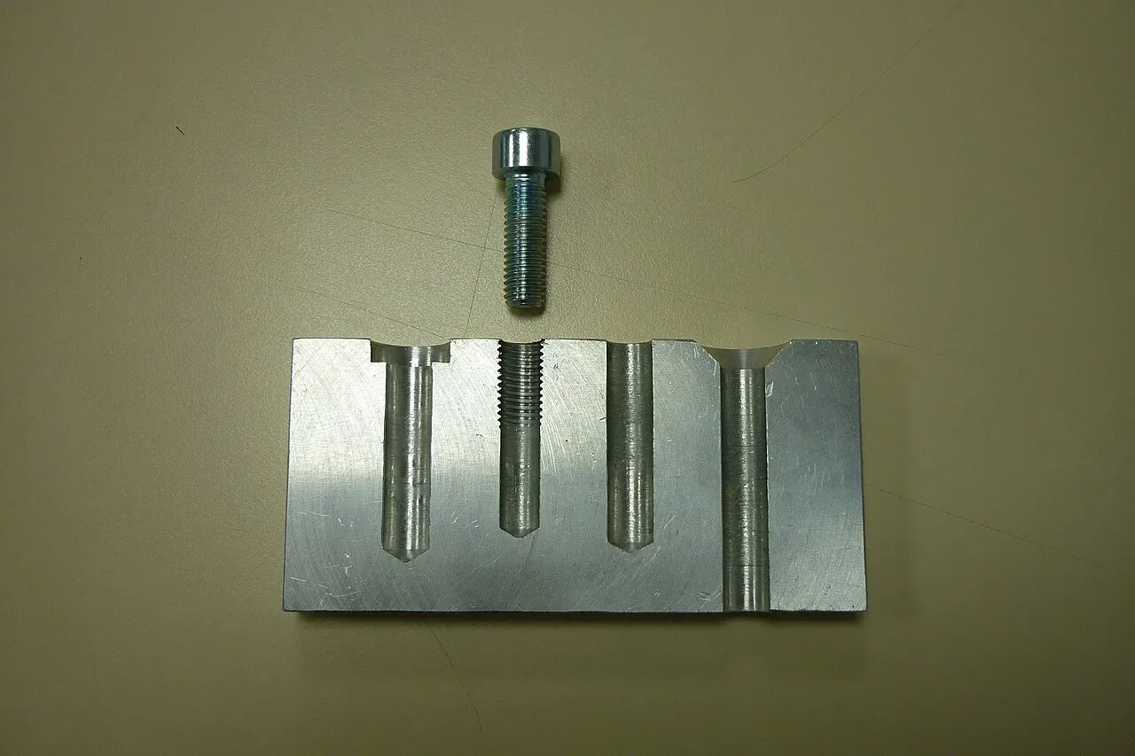 Aluminium block cut in half to show a tapped hole beside drilled and counterbored holes, with a cap screw above