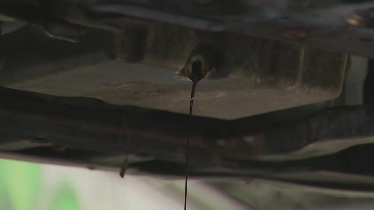 Used engine oil draining in a thin stream from a sump plug under a vehicle