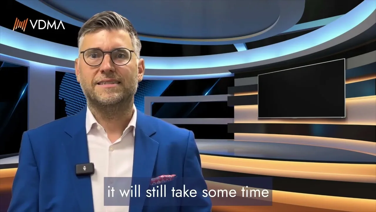 VDMA presenter in a studio with the caption 'it will still take some time', from the July production forecast video